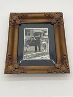 Rectangular vintage bubble picture frame with a gold-tone ornate corner design, showing a black and white photo underneath. The bubble glass distorts the image. Frame edges show wear and one corner is separating.
