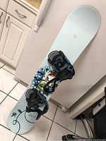 Full snowboard with rear view of bindings showing floral graphic detail and black and blue bindings.