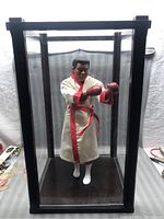 The full figure standing inside the black-framed glass display case, showing the boxing pose and robe.