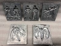 Full view of the 5 DC Comics metal molds placed on a dark surface showing embossed Batman and Superman figures and dates.
