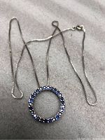 Full view of the silver necklace with circular pendant showing front stones, laying on light fabric background.