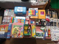 Full overview of all art and craft supplies laid on table including markers, brushes, coloring books, and craft accessories