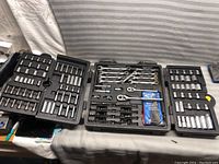 Three open plastic cases displaying the Husky tool set with sockets, bits, wrenches, and ratchets laid out on a table.