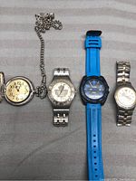Full view of four watches in the lot showing the pocket watch with chain and three wrist watches including metal and silicone bands