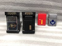 Four Zippo lighters on display, two in stand holders with brand name, showing different designs including 40th anniversary and black with brass accent.