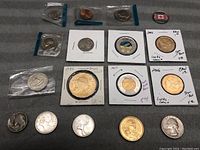 View of multiple coins including Canadian coins encased in holders, silver coins, and a gold-colored coin from 1984 Royal Canadian Mint.