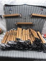 Photo showing large pile of wooden coat hangers with metal clips stacked on each other, three hangers hung above for display.