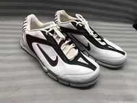 Front angled view of the shoes showing white upper with black and red design and Nike swoosh on side.