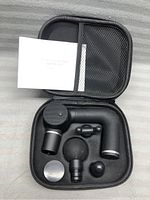 Black handheld Pirouette massage gun with four different massage heads and charging cable in a black zippered carrying case with mesh pocket, shown with user manual.