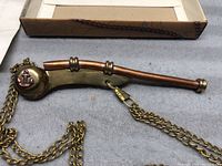 Bosun's whistle laid out with chain, box in background on surface.