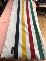 Full view of vintage wool Hudson Bay blanket with navy blue, yellow, red, and green stripes on white background.