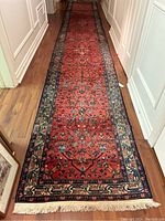 Full-length view of runner laid in hallway showing red field, navy border and ivory fringe at one end
