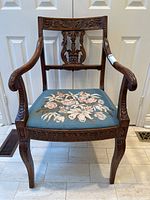 Full front view of carved oak armchair with floral needlepoint seat