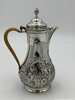 Front-side view showing overall form, hinged lid with finial, repousse floral panels and rattan handle