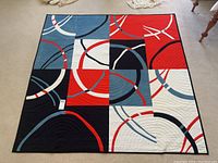 Full view of quilt laid flat showing nine square blocks with curved arc motifs in red, blue, navy and white.