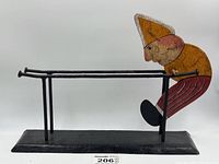 Full view of the metal balancing man on its base showing overall structure, rails and wear