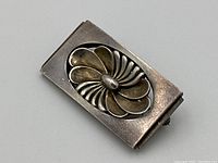 Angled front view of rectangular sterling silver brooch showing raised swirling floral motif and patina