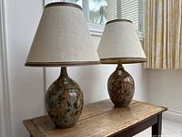 Both pottery table lamps with shades on wooden surface