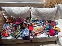 Overview of approx. 30 folded scarves in various colors and patterns displayed on a white sofa