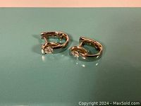 Pair of small hinged hoop earrings on teal surface showing overall design and finish