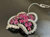 Front view of brooch on black surface showing ruby and diamond arrangement with safety chain visible