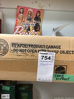 Cardboard shipping box with a label marked 'Barbie' and a Barbie Magazine visible in the background.
