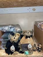 Two large plush Boyd's Bears figures with tags, one in black velvet and leopard hat, the other in tan sweater and gray pants.