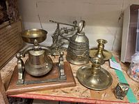 Full view of set on shelf showing large mounted bell on wooden base, large ornate brass bell, candlesticks, and goblet.
