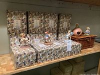 Overview of Cherished Teddies boxes with some figurines placed on top and a wicker basket with two figurines.