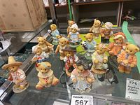 Overview photo of approximately sixteen Cherished Teddies figurines in various costumes and themes displayed on a glass surface.