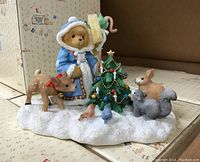 Photo of the porcelain Cherished Teddies Olga figurine standing on a snow base with a Christmas tree, deer, bunny, squirrel, and birds around her.