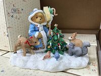 Full view of Cherished Teddies Olga figure in blue coat with lantern and staff standing on snowy base with Christmas tree and animal companions including deer, rabbit, squirrel, and birds.