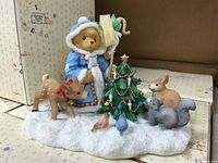 Overall display showing teddy bear Olga in blue coat, small deer, decorated Christmas tree, small rabbit, gray squirrel, and bird figurines on snowy base.