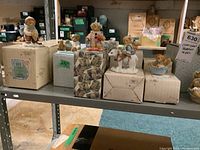 Cherished Teddies resin figurines displayed on shelf, many boxed and some unboxed sitting on top.