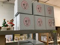 Six boxed Cherished Teddies figurine boxes stacked on a metal shelf with two displayed bear figurines, showing lot contents and packaging.