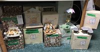 Wide view of Cherished Teddies figurines and original packaging with green tape labels indicating figurine names and styles.