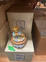 Photo of Cherished Teddies musical bear figurine in blue pajamas kneeling on pastel patchwork cushion with smaller teddy bear, on round wooden base with blue ribbon detail.