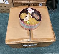 Round metal cookie tin with clear lid showing a yellow plush teddy bear and a small figurine teddy bear inside the tin. Labels visible indicating Cherished Teddies Gift Set with included figurine, plush teddy, and cookie tin.