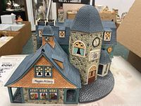 Full view of the Department 56 Bay Street Shops ceramic building showing Maggie's Millinery store and stone clock tower.