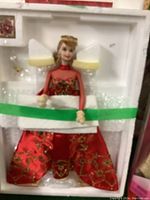 Holiday Barbie Porcelain Edition doll in original protective white foam and plastic packaging with green tape securing the doll. Doll is dressed in a red gown with gold and green embroidery and bead detailing. Blonde hair styled, wearing red earrings and red choker.
