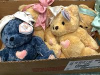Four Precious Moments plush teddy bears together in a cardboard box, showing different colors and ribbons