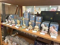 Shelf displaying approximately 13 Precious Moments Birthday Train collectible figures on wheeled bases lined up, with some original blue boxes behind them.