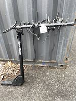 Black metal SportRack bike carrier holding 4 bicycles with adjustable straps, shown upright against a container wall.