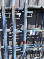 Close view of blue scaffolding frames highlighting two safety bar brackets and areas of surface rust