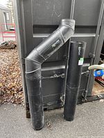 Black double wall stove pipes including a telescoping piece, elbow joints, and straight pipes arranged outside.