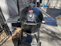 Front view of Char-Griller Akorn charcoal kamado grill on cart with foldable side shelves and wheels
