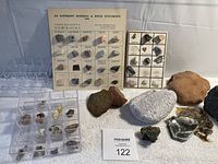 Photo showing assortment of loose rocks and minerals arranged with two plastic display cases and two printed identification cards with mineral names, visible variety and colors.
