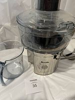 Front and side view of Breville juicer with clear plastic juice catcher and removable measuring jug placed beside it.