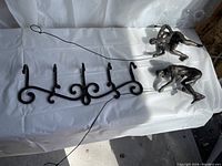 Photo showing the cast iron rack with five hooks and the two climbing men figures lying on a white cloth.