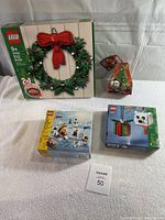 Four LEGO sets in unopened boxes: large wreath set in green packaging, two small ornament boxes including a Christmas tree shaped box, and a winter scene set with snowy landscape.